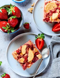 Pieces of strawberry crunch cake on plates with strawberries.