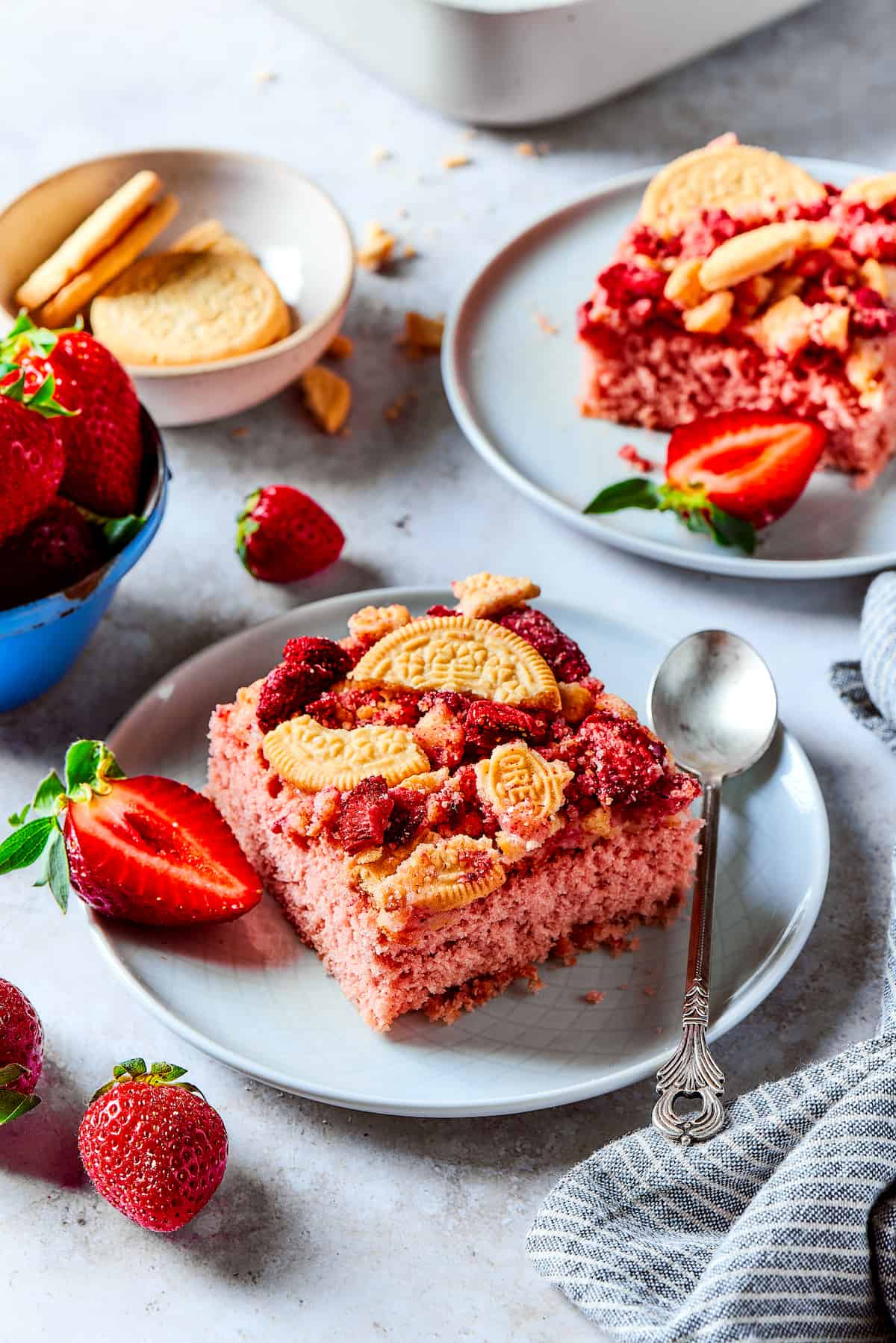 Pieces of strawberry crunch cake on plates with strawberries in bowls.