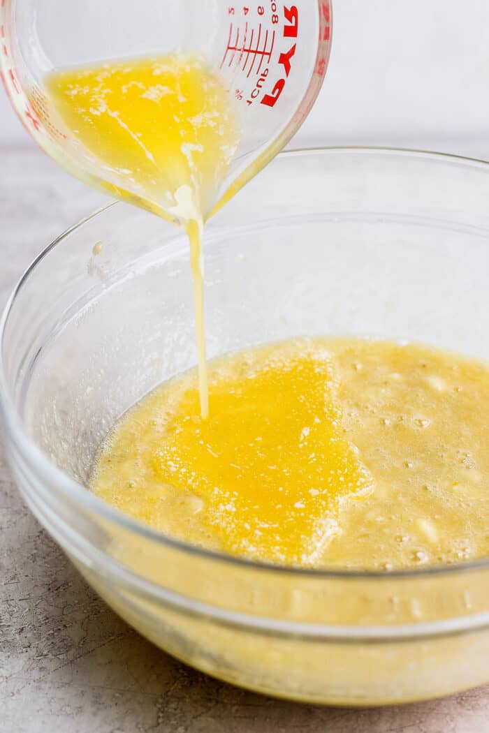 pouring melted butter into a clear bowl with mashed bananas