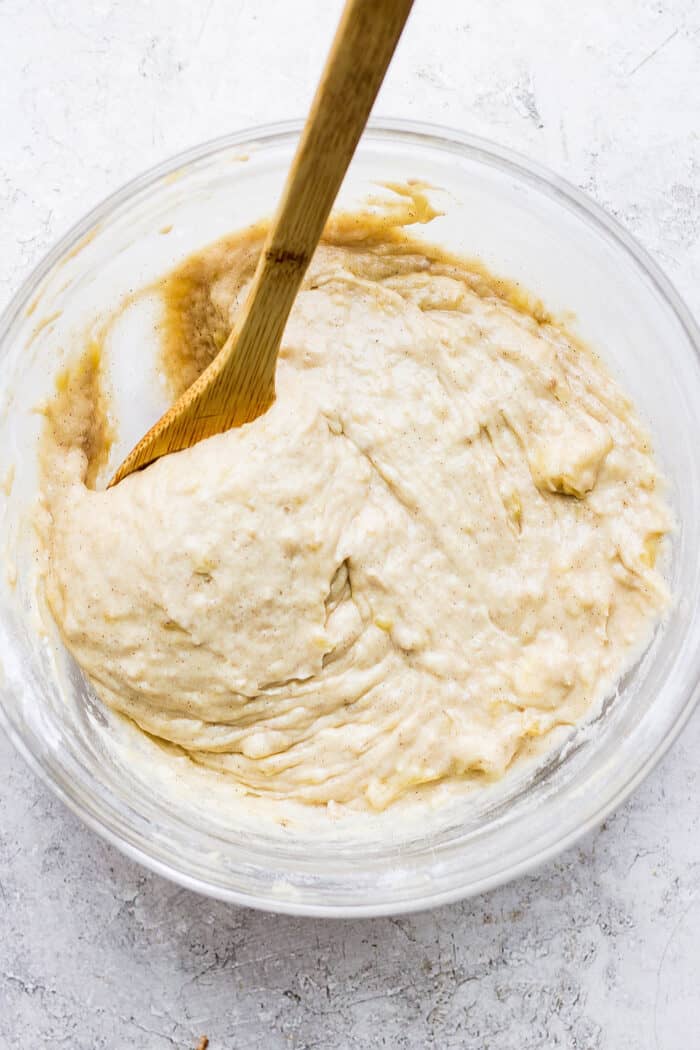 banana muffins batter in clear bowl, with wooden spoon