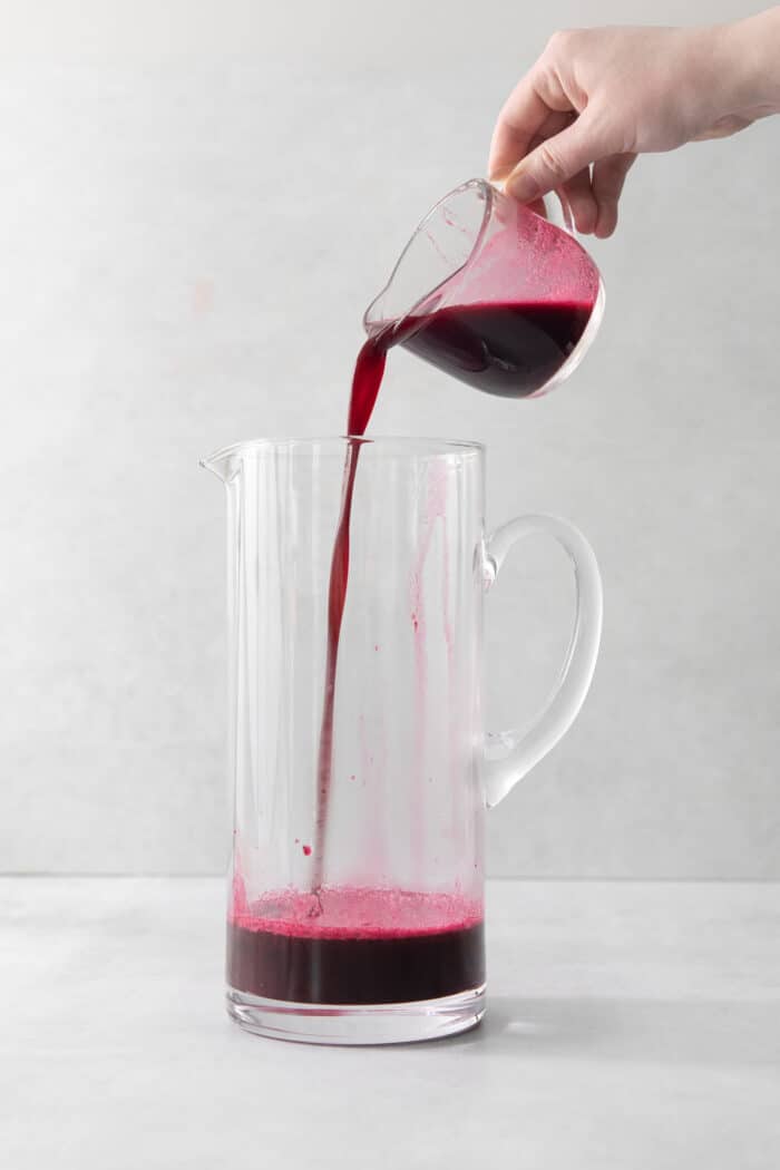 A cup pouring blueberry syrup into a pitcher