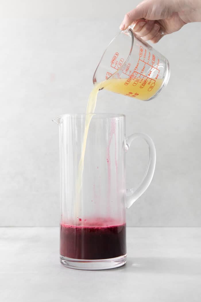 Lemon juice being added to a pitcher with blueberry syrup