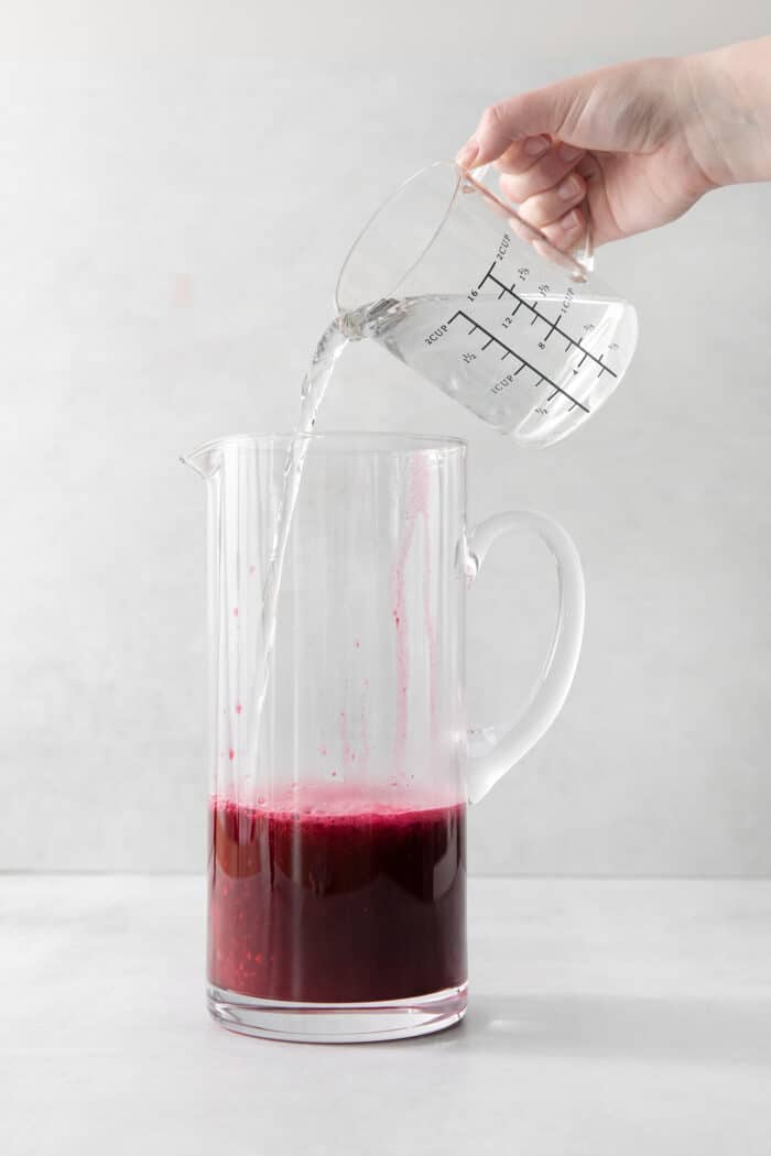 Water being added to a pitcher with lemon juice and blueberry syrup