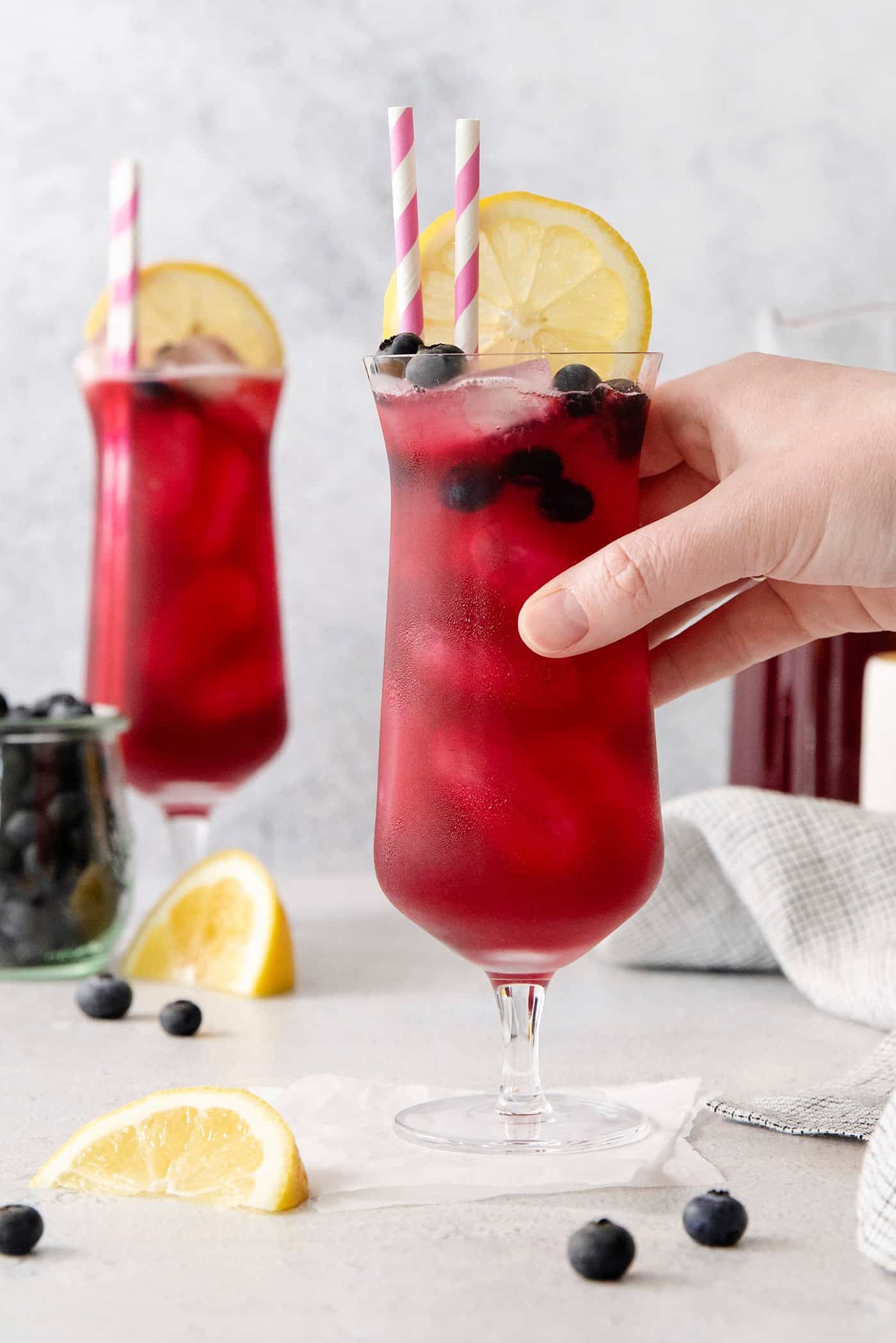 A hand grabbing a glass of blueberry lemonade