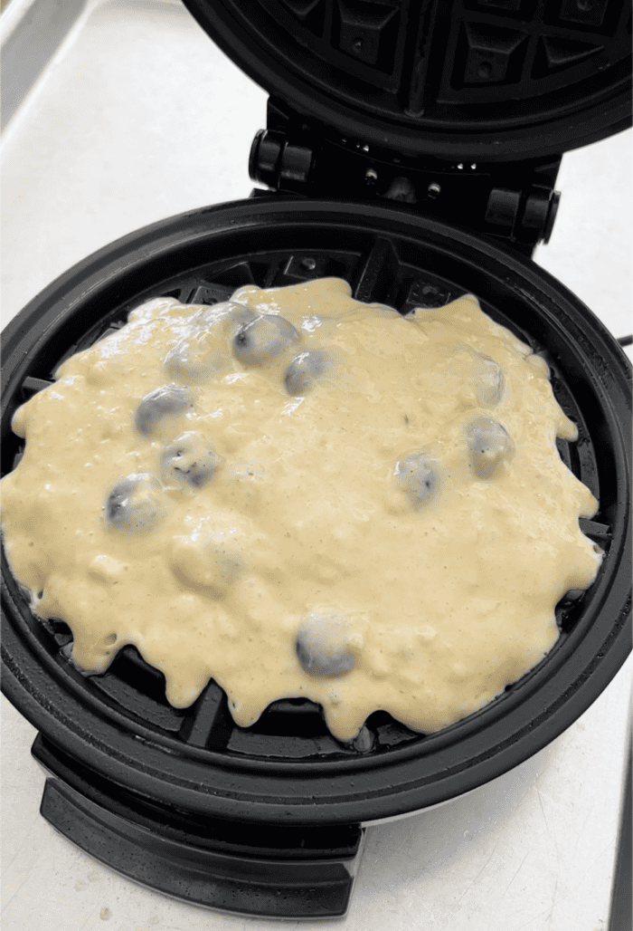 waffle batter with blueberries in a waffle maker
