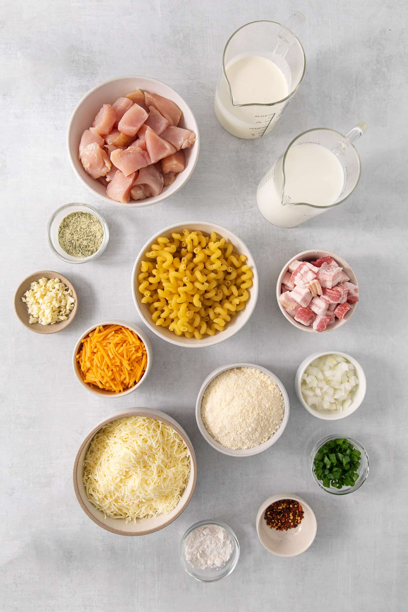 Ingredients needed to make chicken bacon ranch pasta are shown, including pasta, chicken, cheeses, bacon, and green onions.