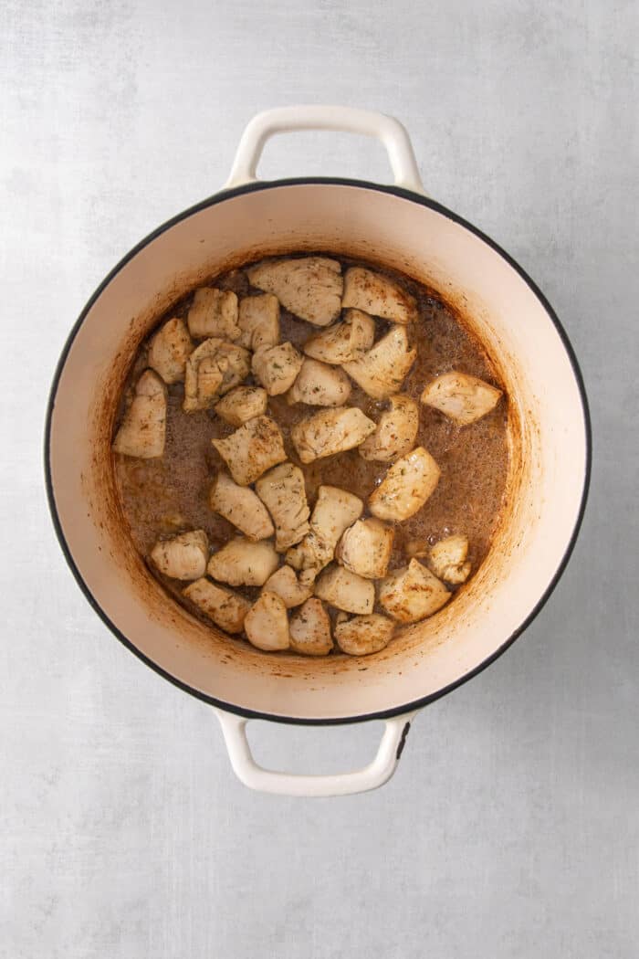 Pieces of chicken are added to a pot to cook.