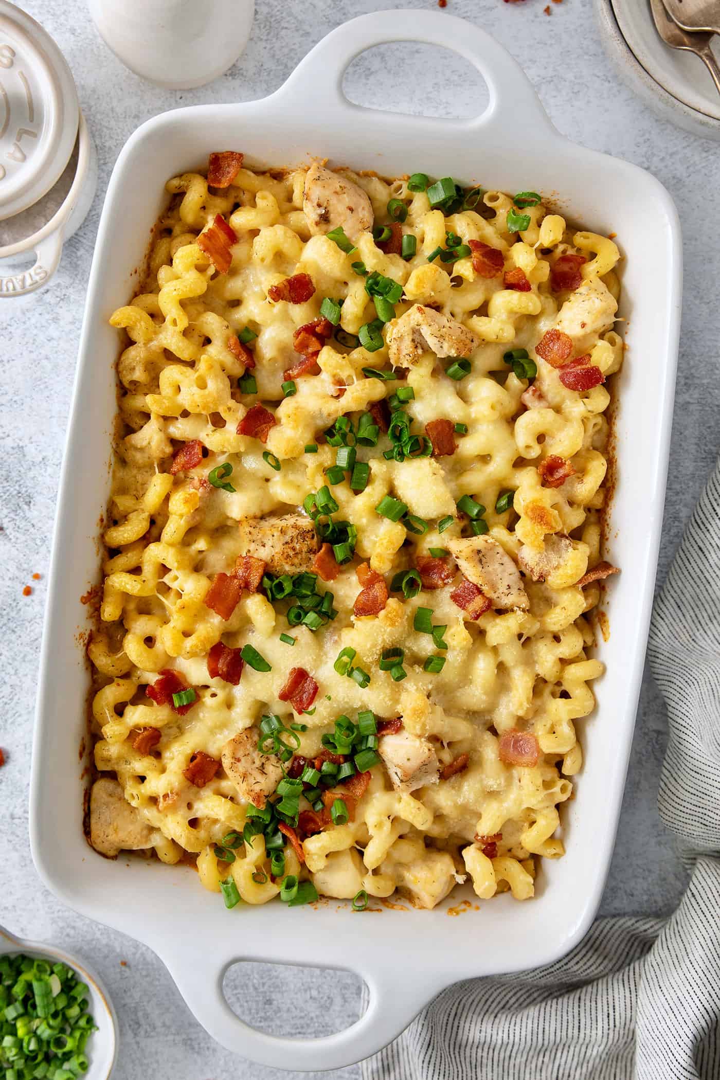 A baking dish is full of chicken ranch pasta covered with sliced green onions, chicken, and bacon.