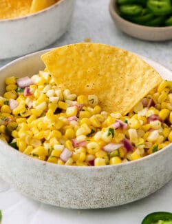 A tortilla chip in a bowl of corn salsa