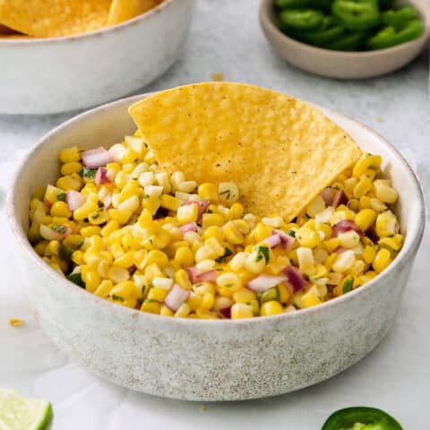 A tortilla chip in a bowl of corn salsa
