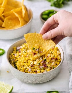 A hand using a tortilla to scoop up roasted chili corn salsa