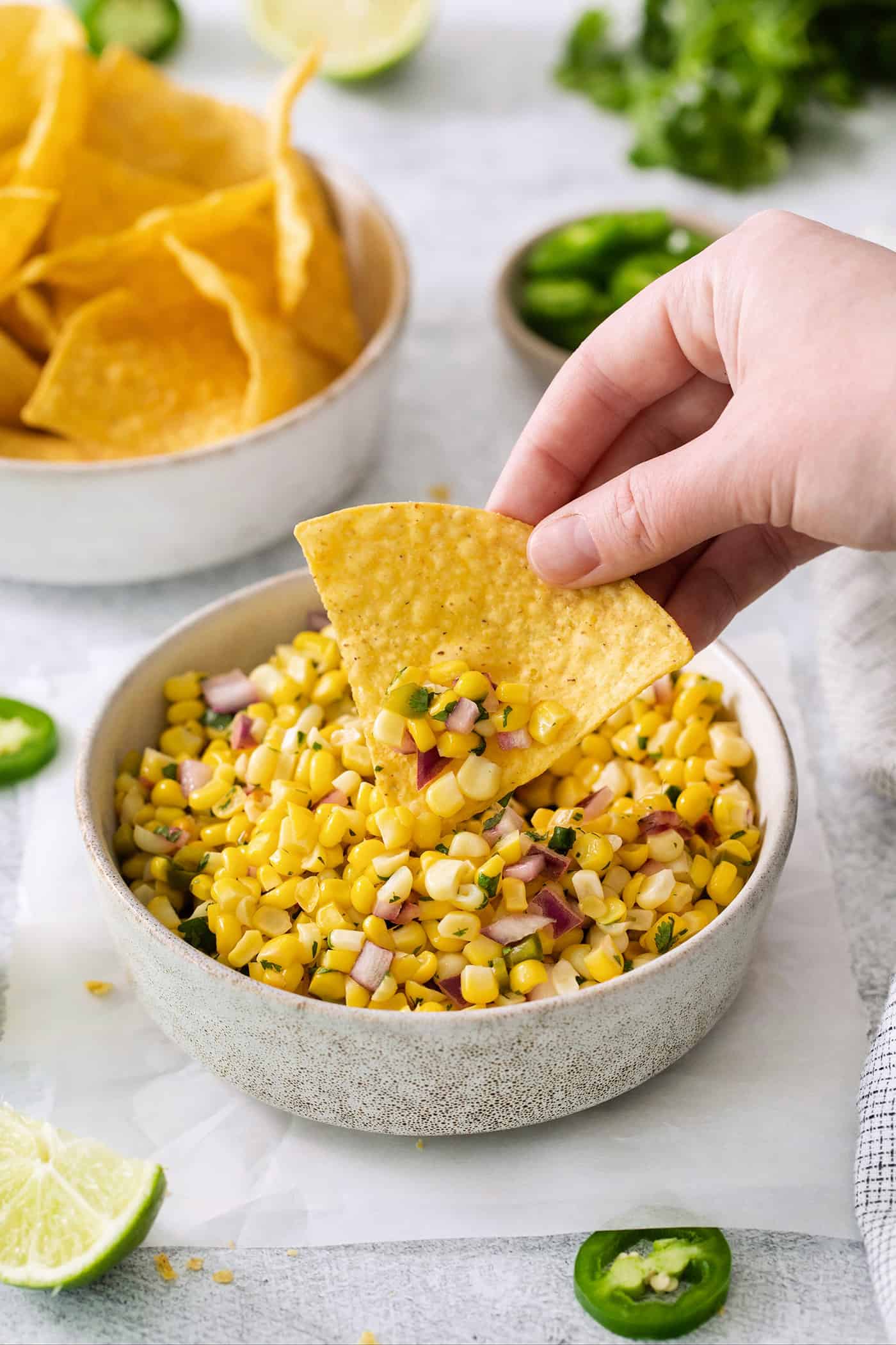 A hand using a tortilla to scoop up roasted chili corn salsa