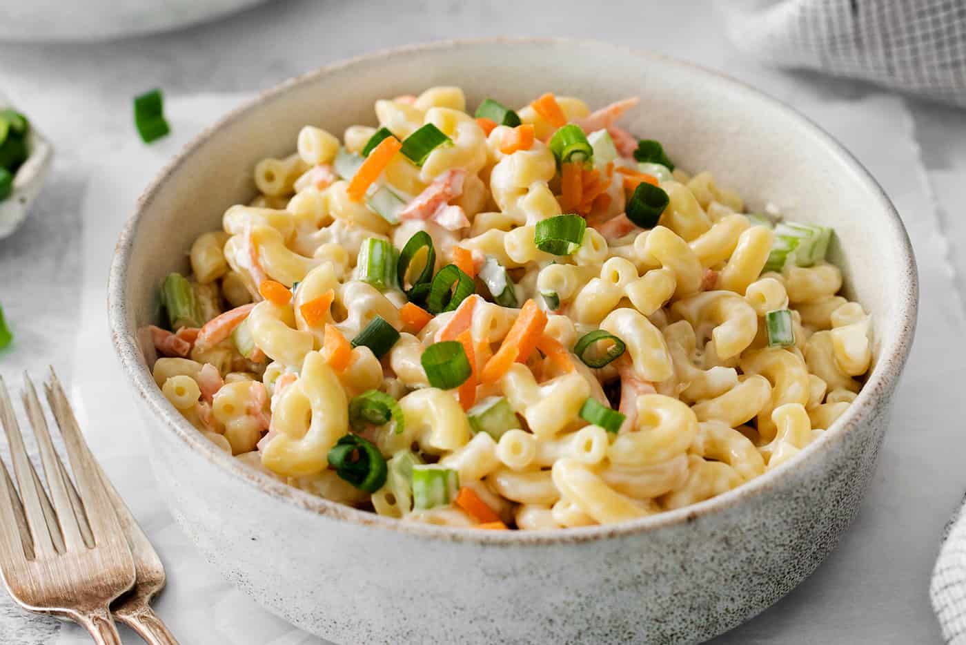 A close up shot of hawaiian macaroni salad topped with chopped vegetables.