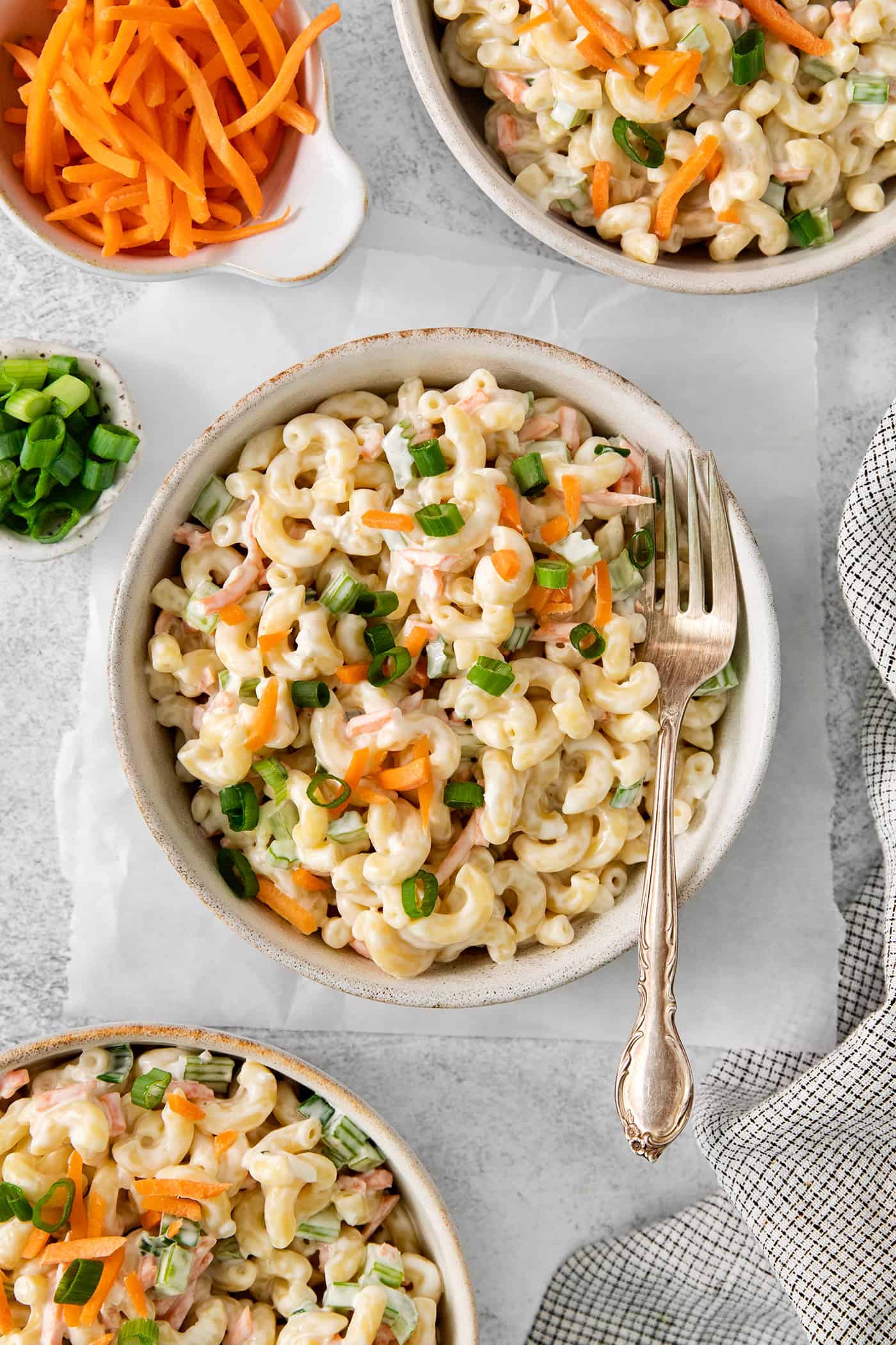 Bowls of hawaiian macaroni salad are seen in white bowls on a table with forks.