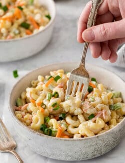 A fork digs into a white bowl of hawaiian macaroni salad on a table.