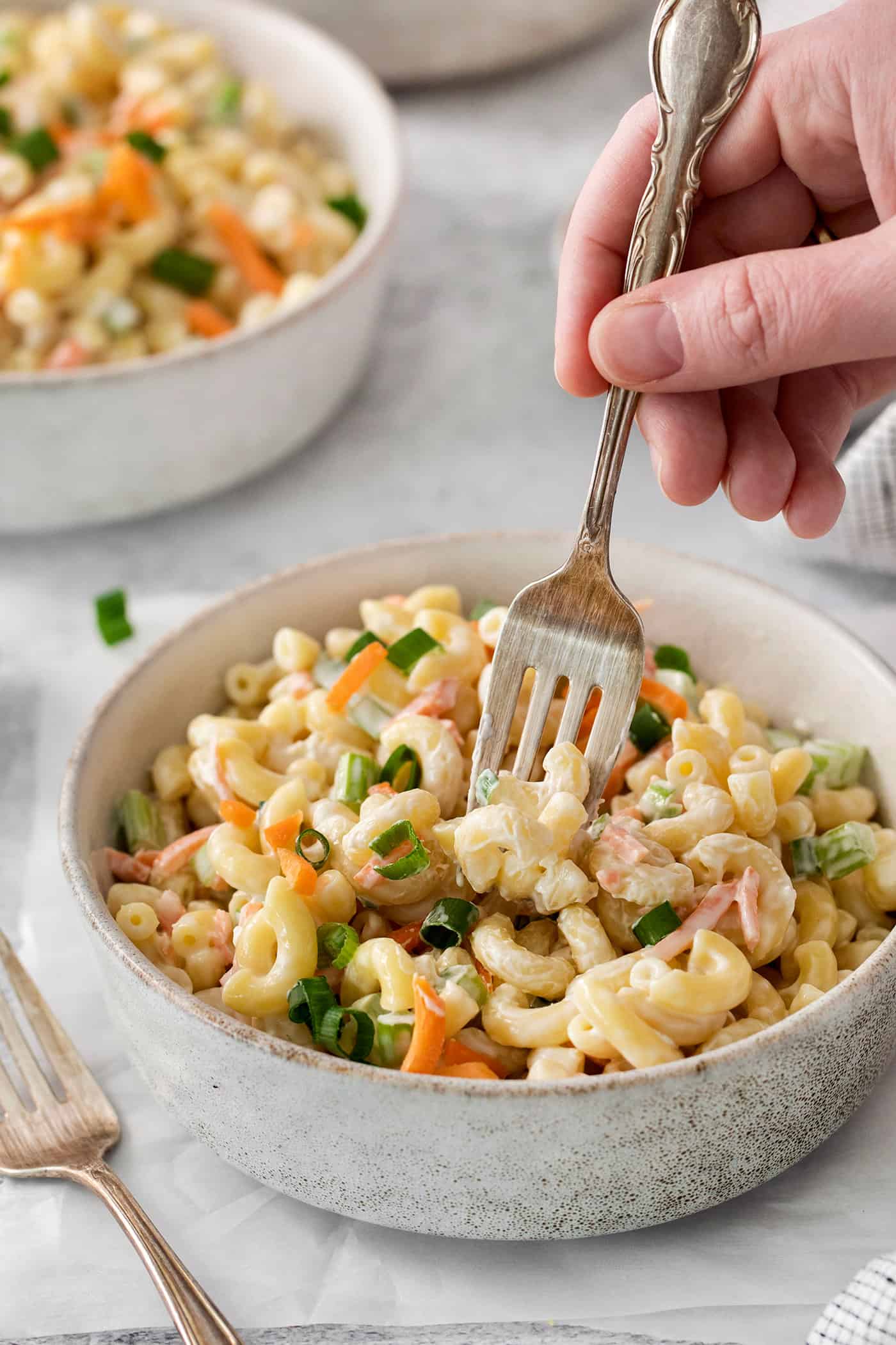 A fork digs into a white bowl of hawaiian macaroni salad on a table.