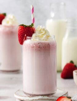 Glasses of strawberry milk with milk in the background.