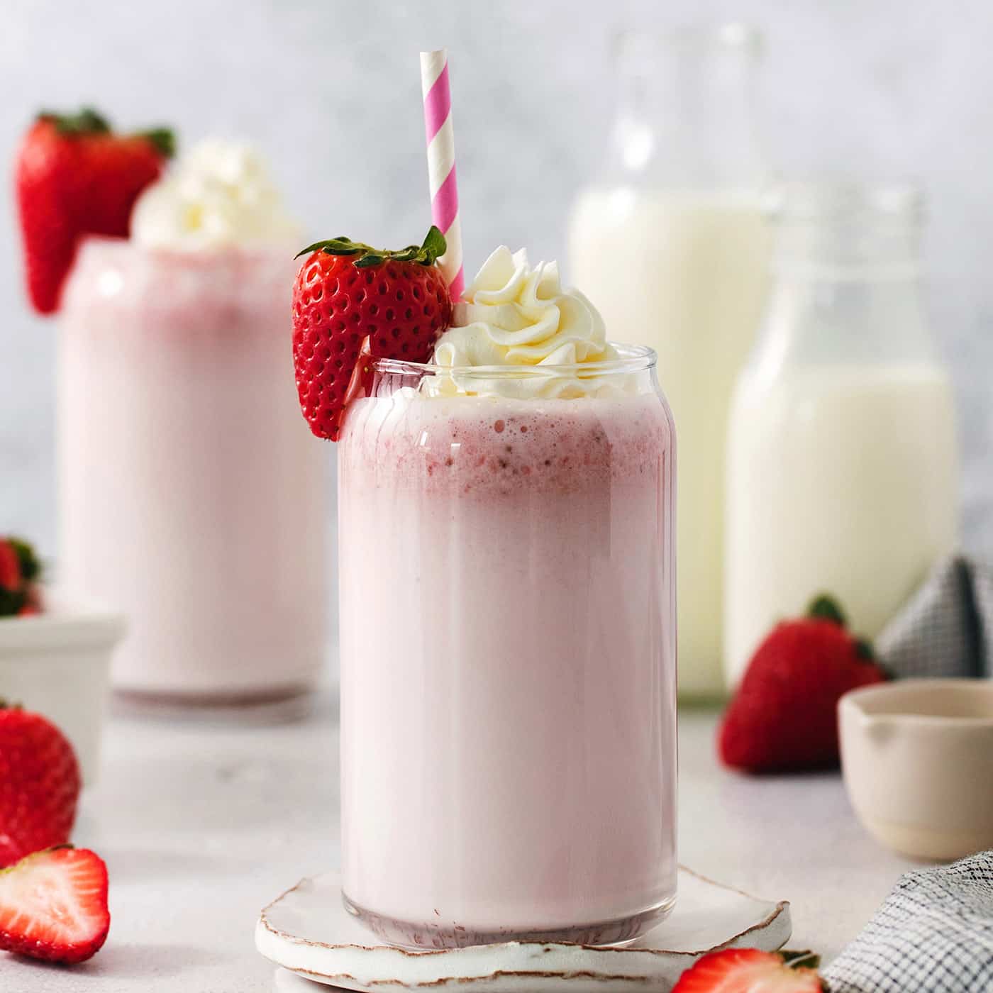 Glasses of strawberry milk with milk in the background.