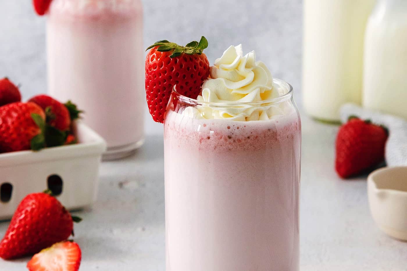 Glasses of strawberry milk with milk in the background.