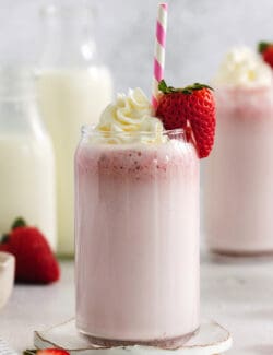 Glasses of strawberry milk with milk in the background.