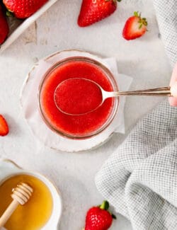 a spoon of strawberry sauce coming out of a jar of strawberry sauce