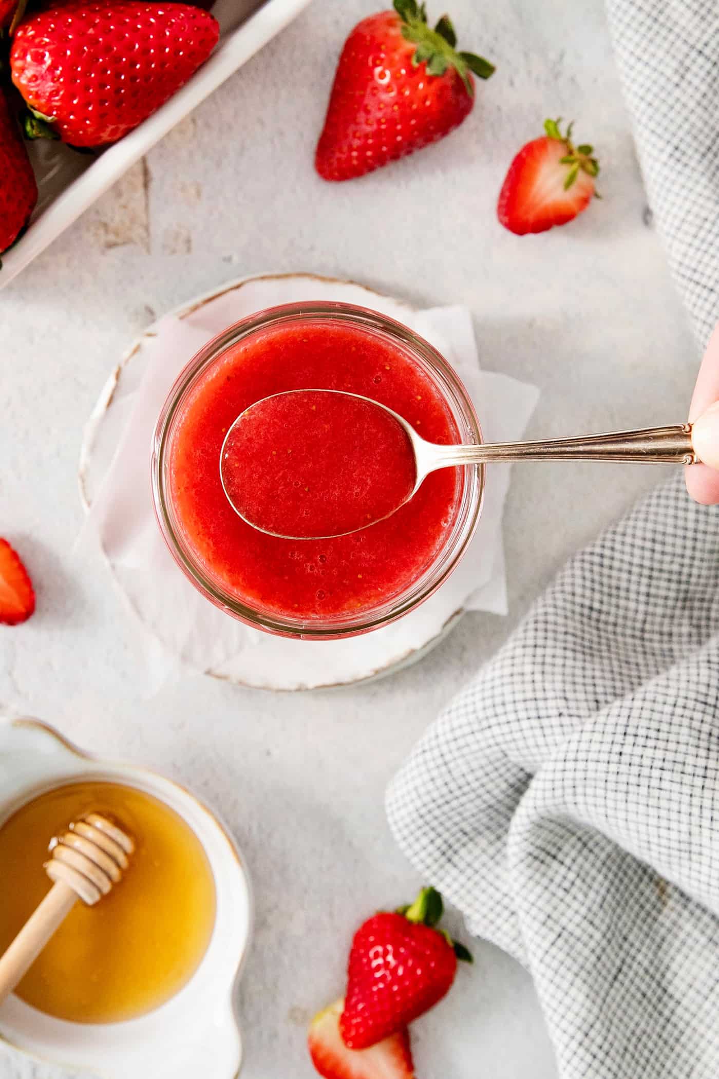 a spoon of strawberry sauce coming out of a jar of strawberry sauce