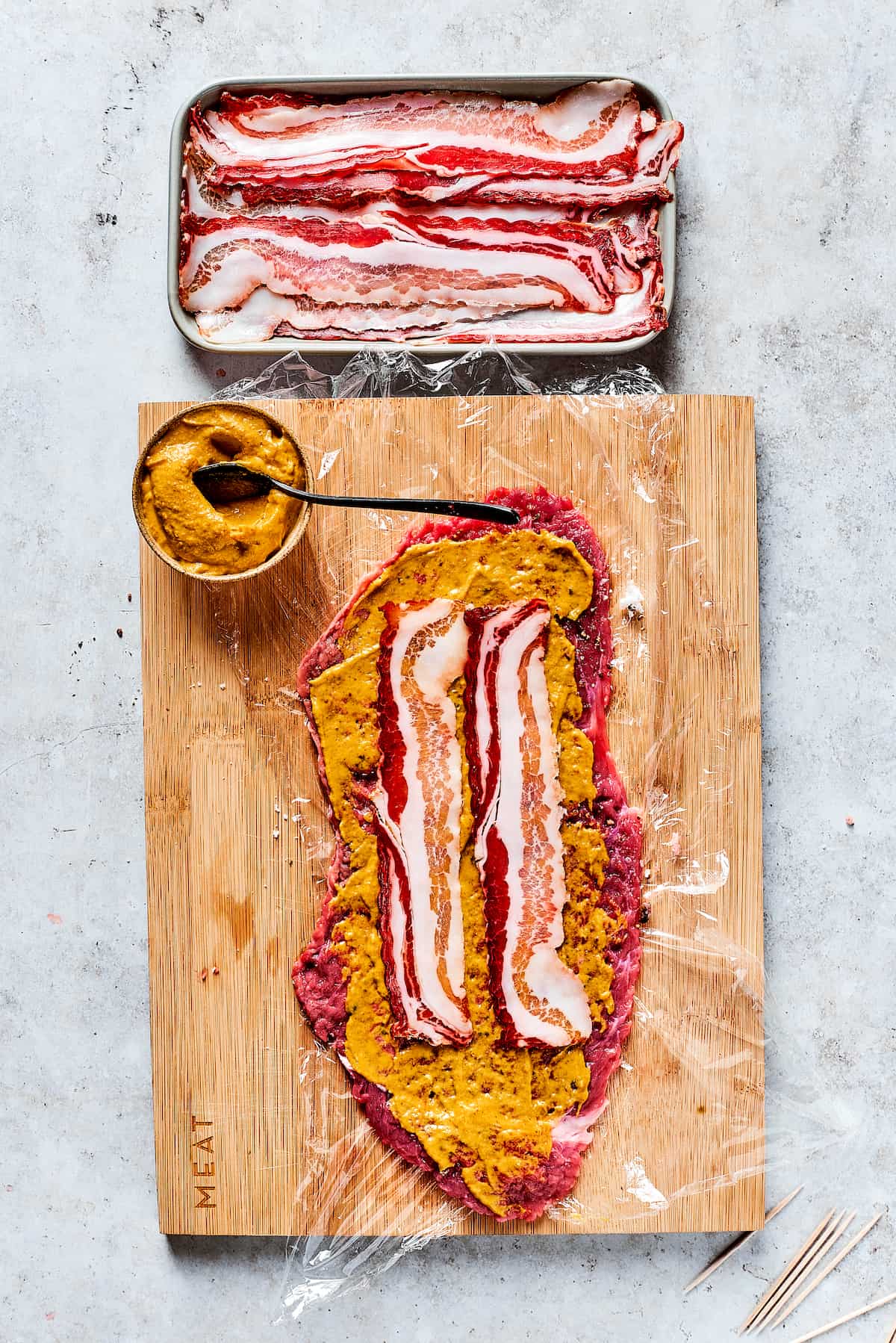 Adding bacon and mustard to a beef strip.