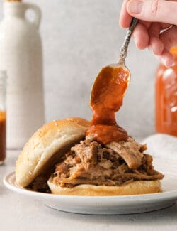 spooning bbq sauce onto a shredded pork sandwich