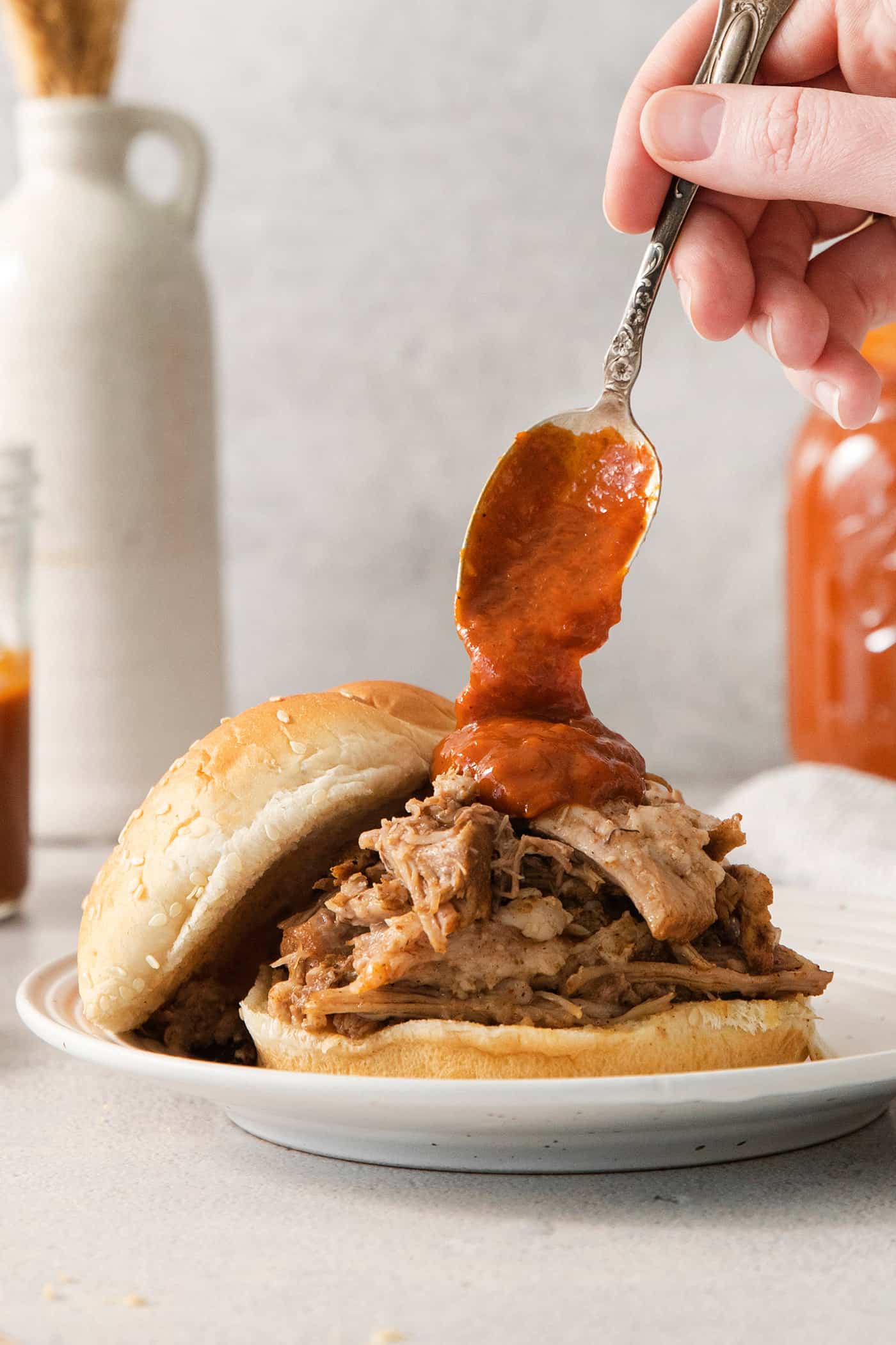 spooning bbq sauce onto a shredded pork sandwich