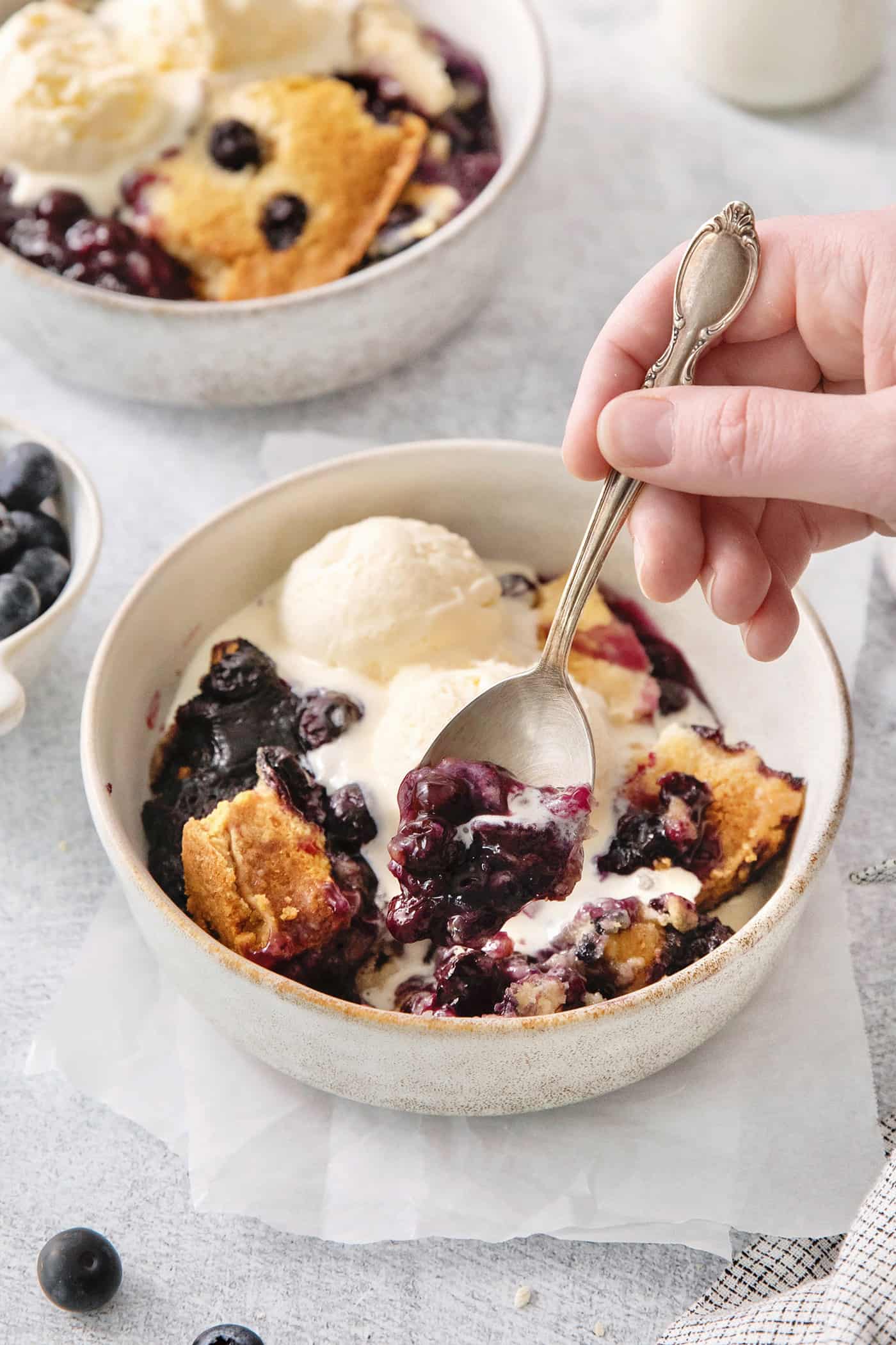 A hand holds a spoon dipping into a bowl of blueberry dump cake.