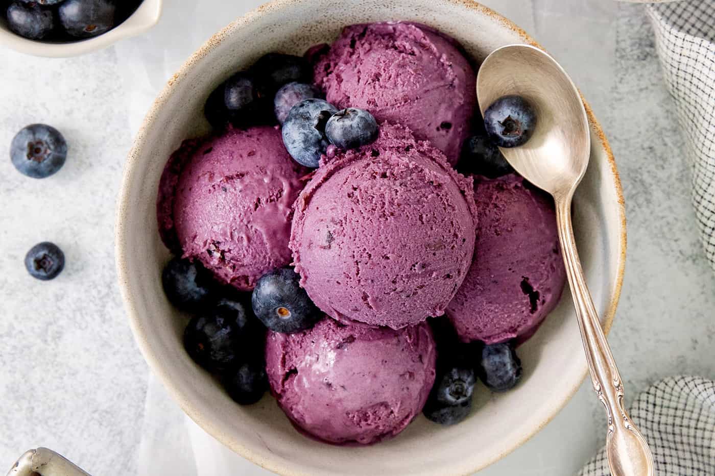 A bowl of scoops of blueberry ice cream with a spoon.