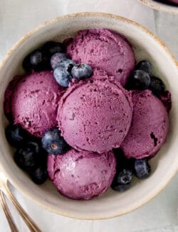 A bowl of scoops of blueberry ice cream with a spoon.