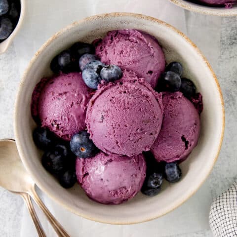 A bowl of scoops of blueberry ice cream with a spoon.