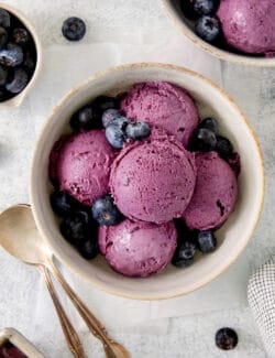 A bowl of scoops of blueberry ice cream with a spoon.