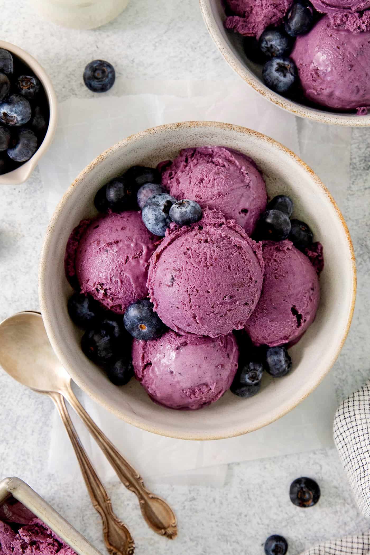 A bowl of scoops of blueberry ice cream with a spoon.