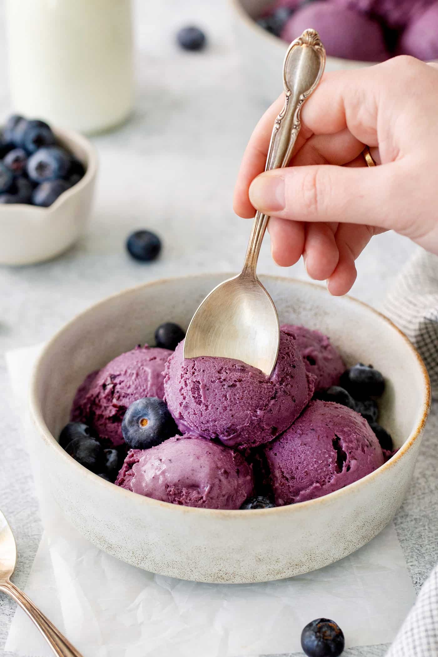 Blueberry ice cream in a bowl with a hand and a spoon.