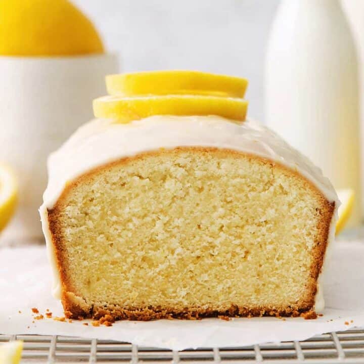 A lemon pound cake on a wire rack with lemons in the background.