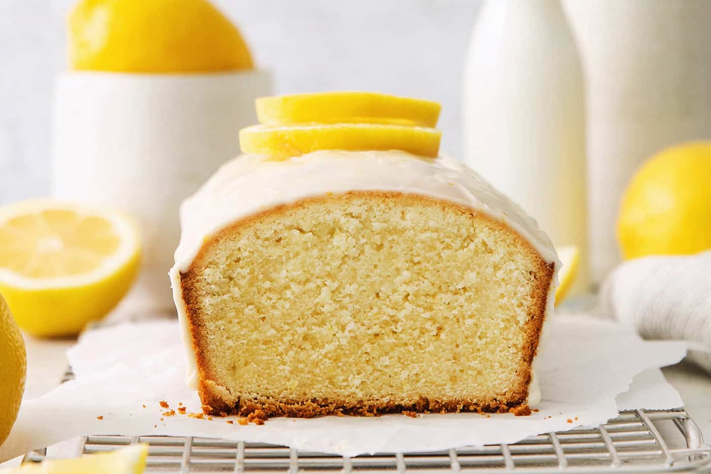 A lemon pound cake on a wire rack with lemons in the background.