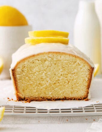 A lemon pound cake on a wire rack with lemons in the background.