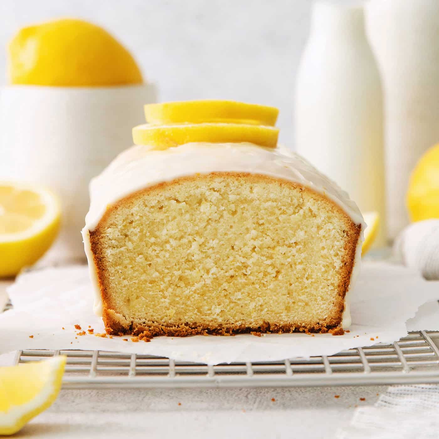 A lemon pound cake on a wire rack with lemons in the background.