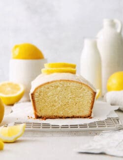 A lemon pound cake on a wire rack with lemons in the background.