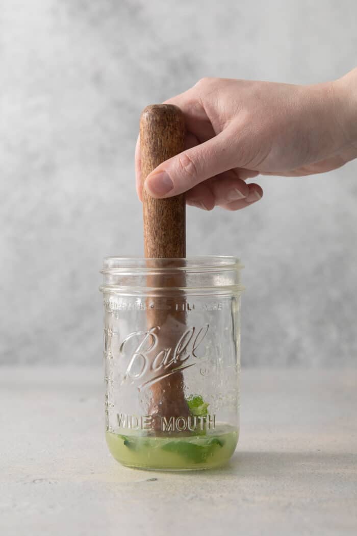 A hand holding a pestle muddles mint.