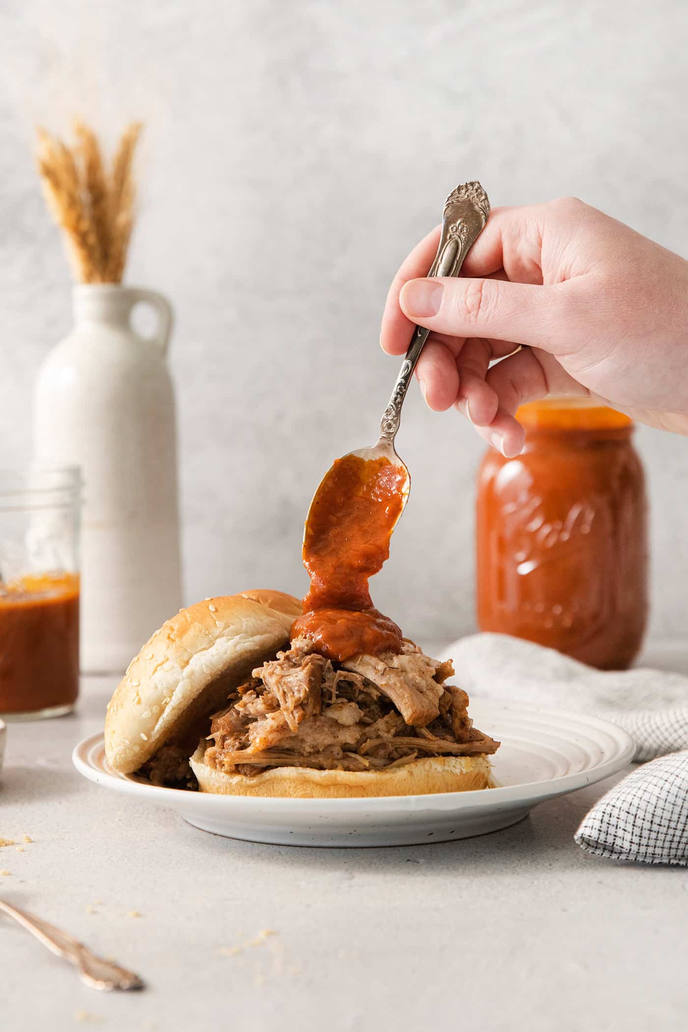 spooning barbecue sauce over a pulled pork sandwich
