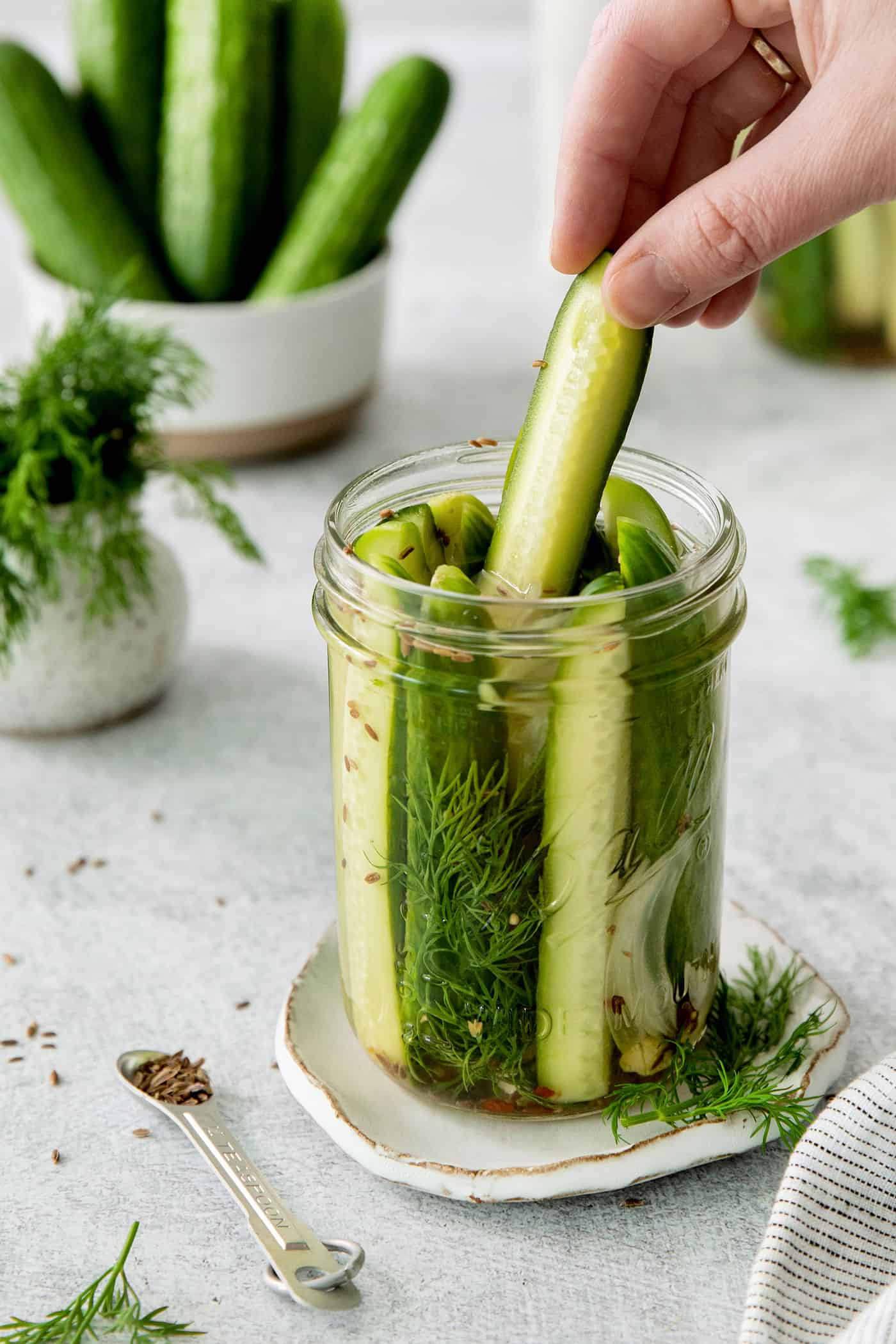A hand pulling a dill pickle spear from a jar