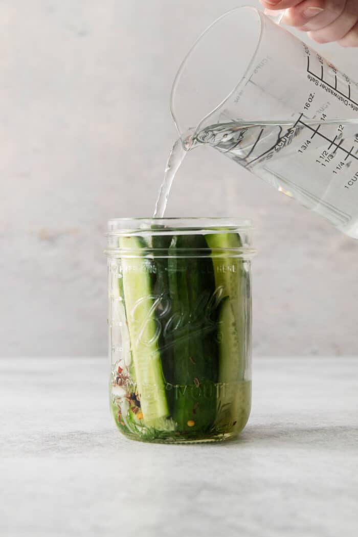 Pickling brine being poured into a jar over cucumber spears