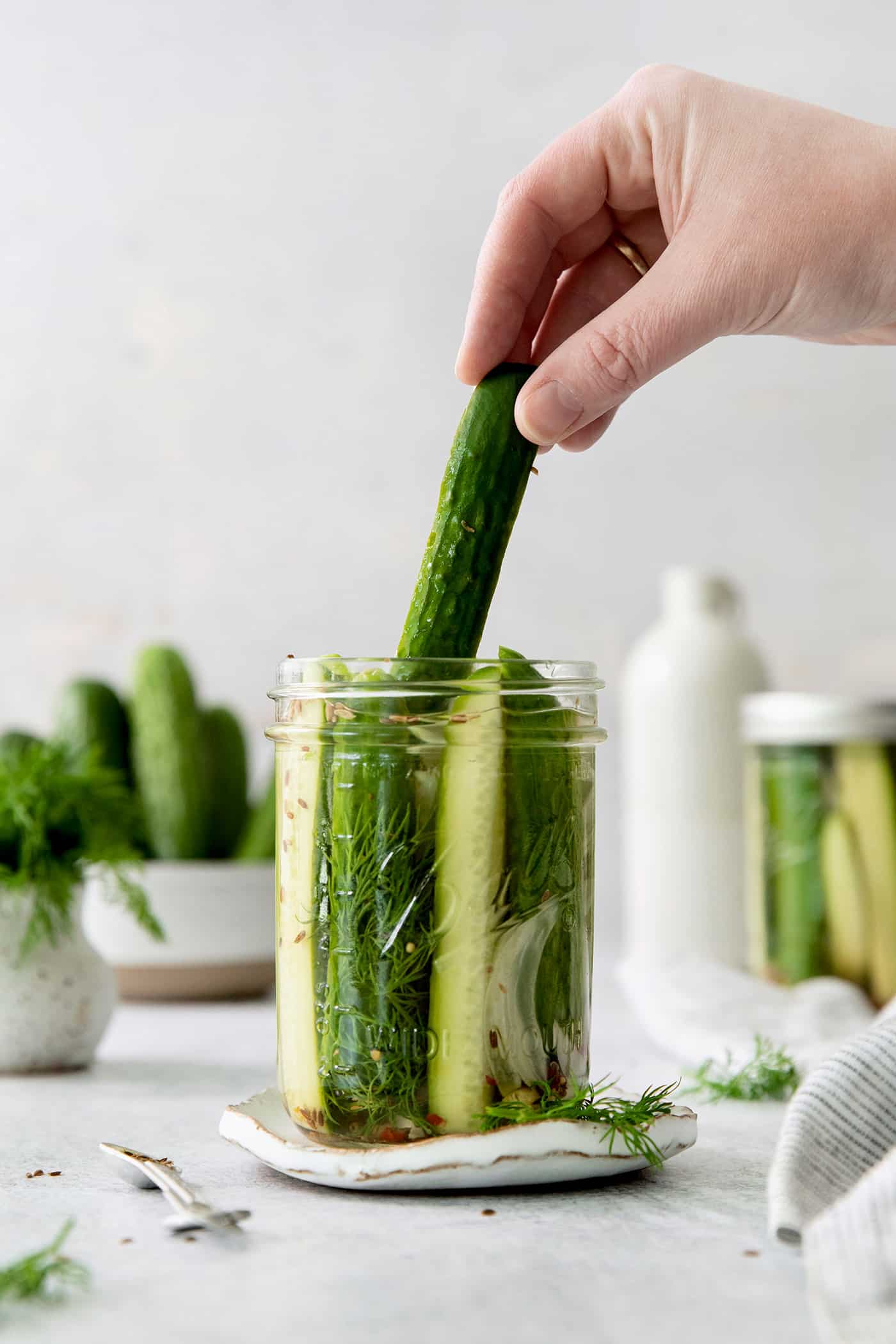 A hand pulling a dill pickle spear from a jar