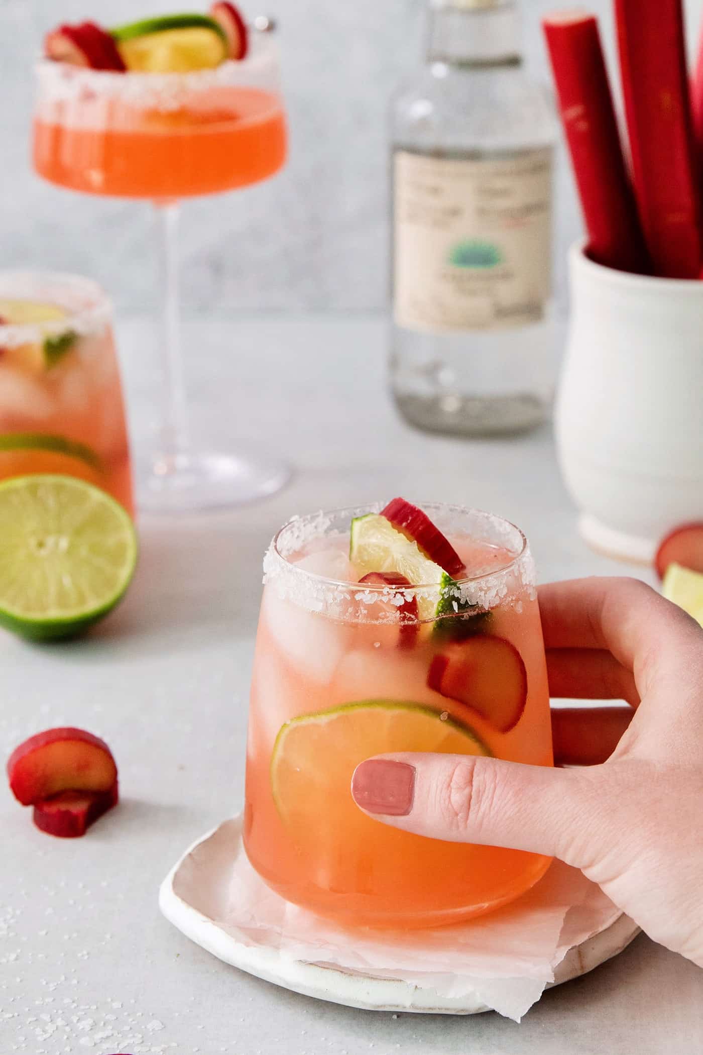 a hand holding a glass of rhubarb margarita