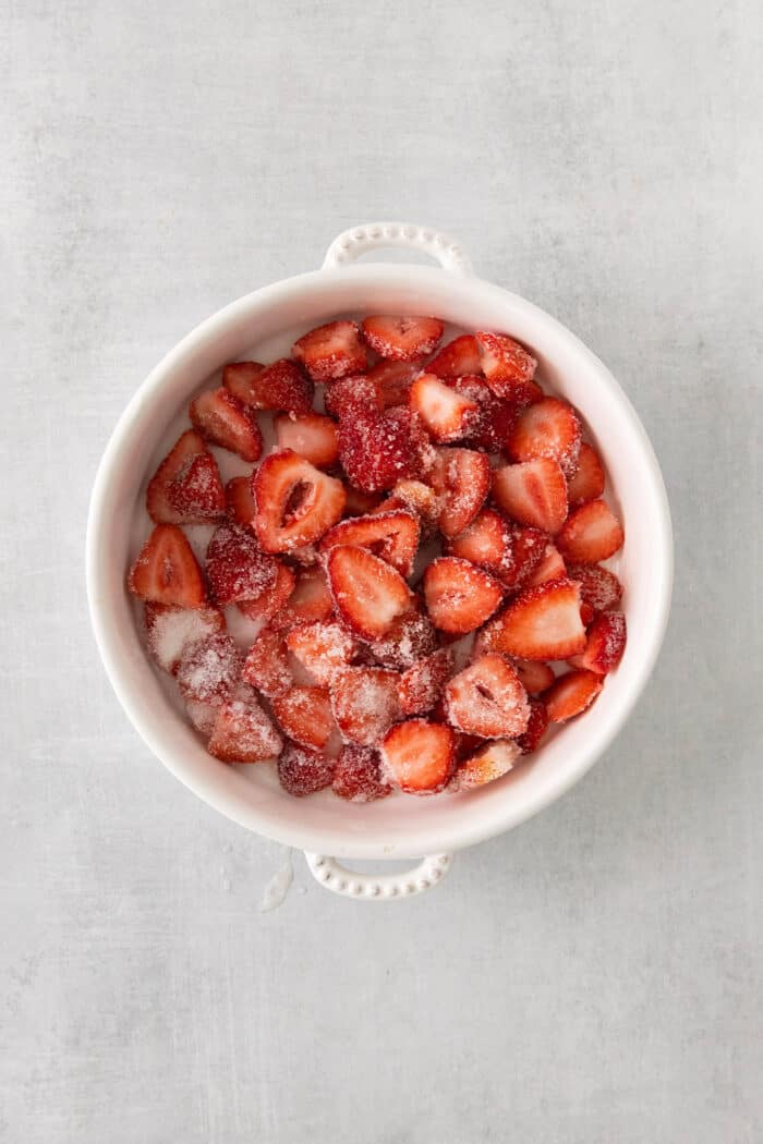 Strawberries mixed with sugar in a white bowl.