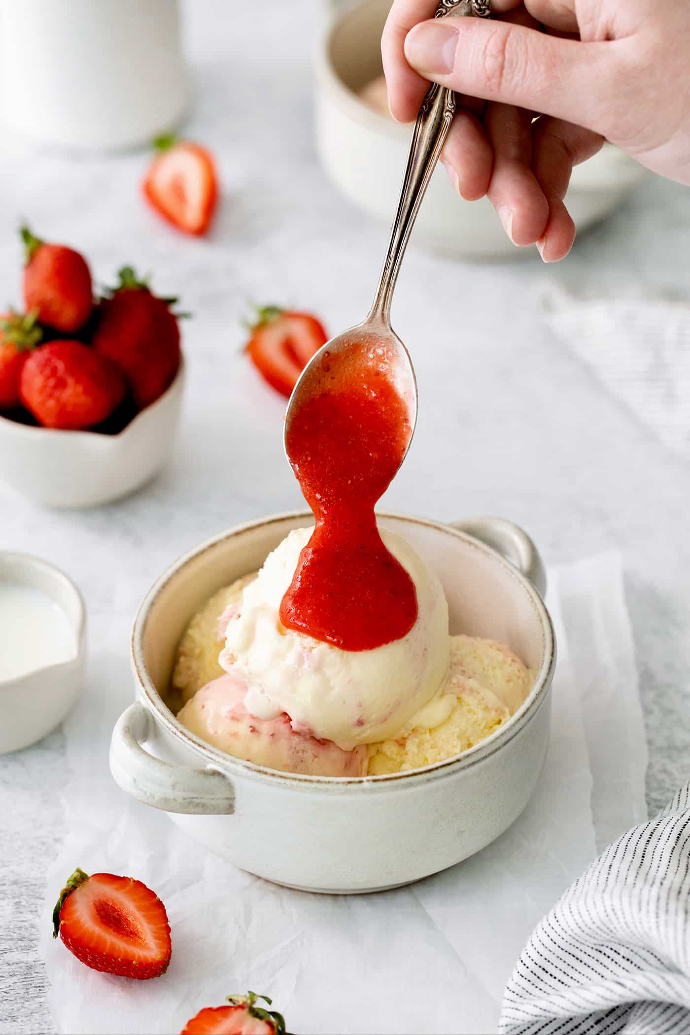 A bowl of crème fraîche strawberry swirl ice cream with a spoon drizzling strawberry sauce.