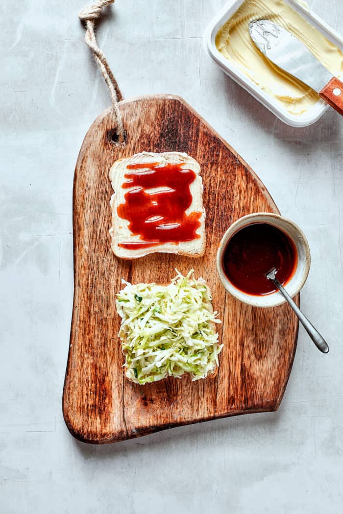 Adding shredded cabbage to bread on a cutting board.